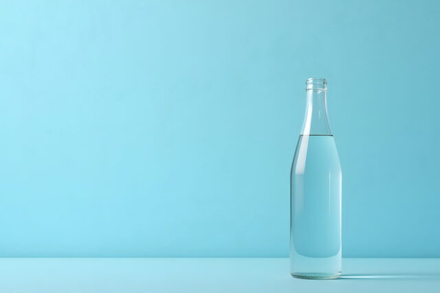 Clear glass water bottle on bright blue background.