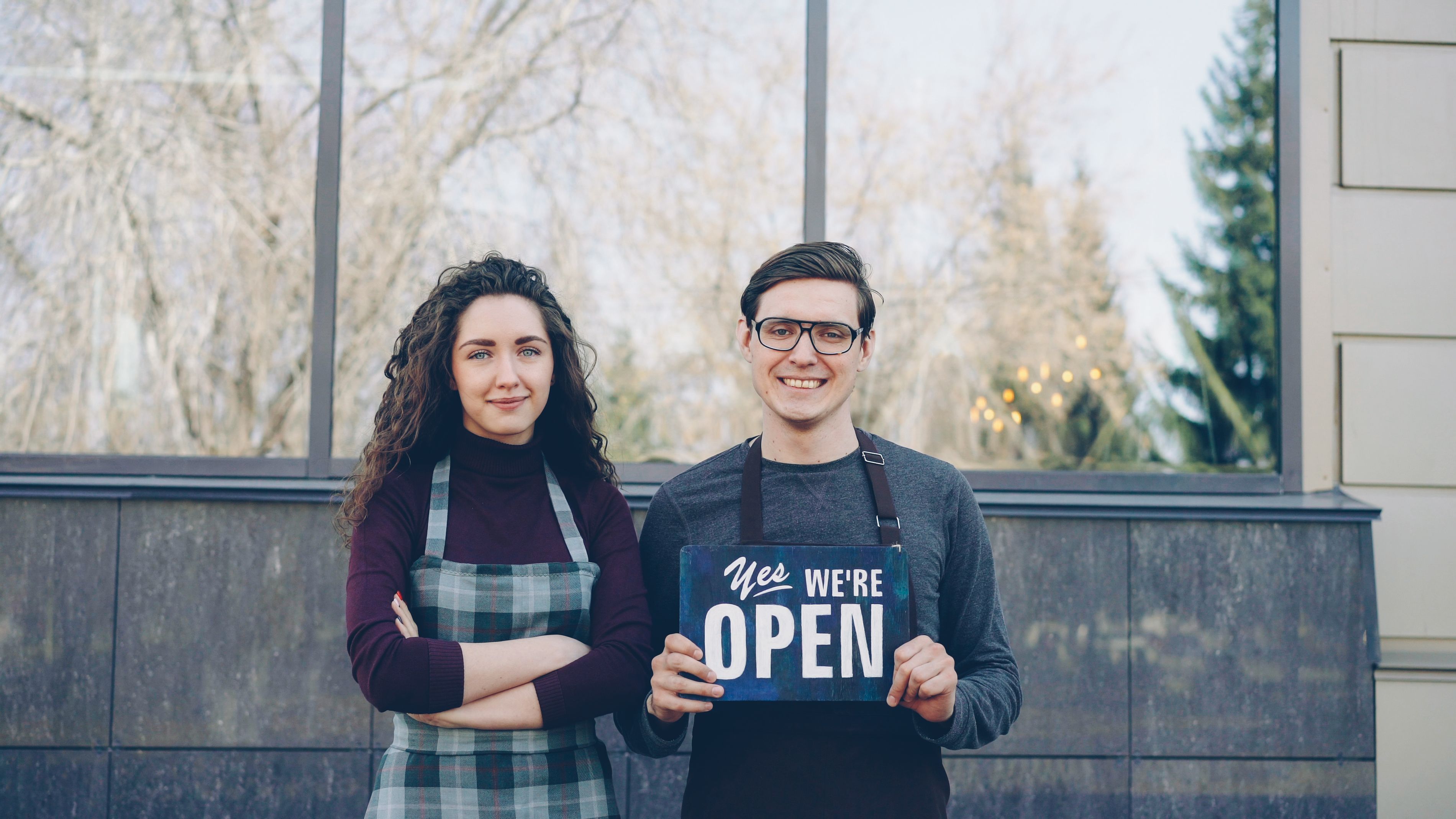 Two local business owners holding an open sign outside their shop to attract nearby customers